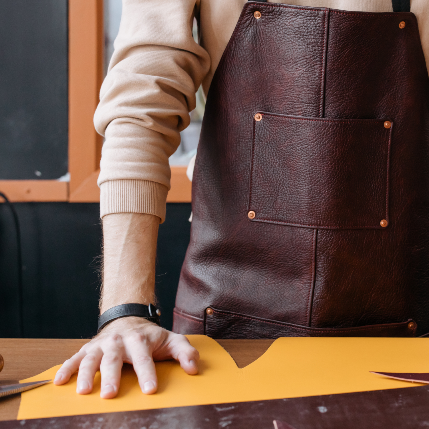 A person wearing a brown leather apron is working with a yellow strap, presumably replacing a strap on a dog collar.