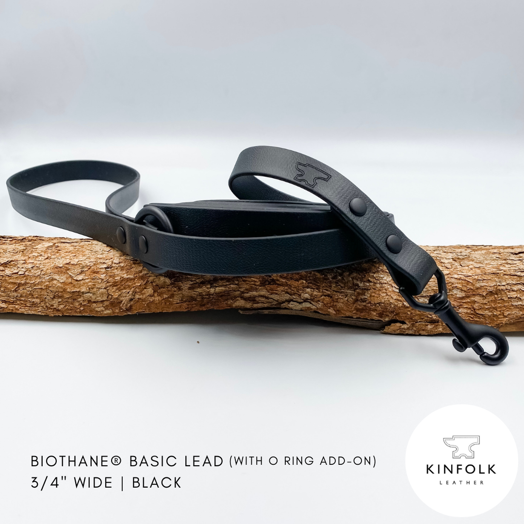Black waterproof biothane dog lead with O ring add-on on a wooden branch against a white background, featuring the Kinfolk Leather logo.