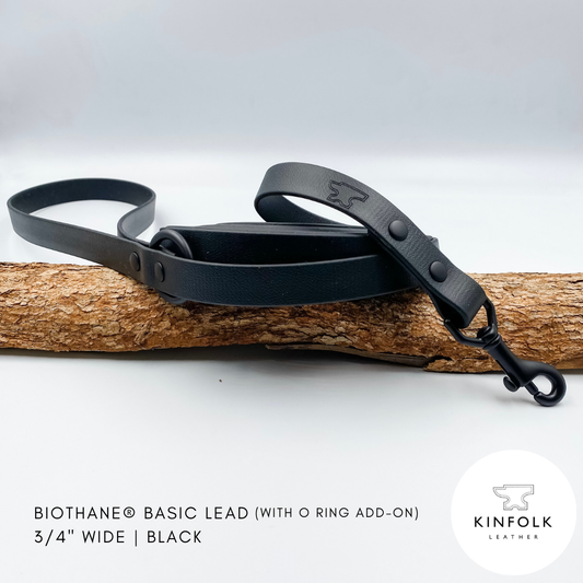 Black waterproof biothane dog lead with O ring add-on on a wooden branch against a white background, featuring the Kinfolk Leather logo.