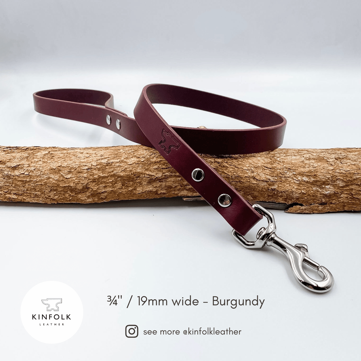 A burgundy leather dog leash with silver hardware, draped over a piece of natural wood on a light gray background. Text at the bottom reads '3/4" / 19mm wide - Burgundy' with the Kinfolk Leather logo and social handle.
