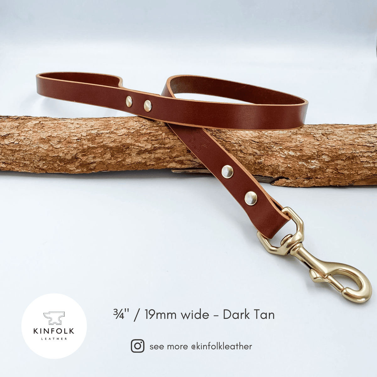 A dark tan leather dog leash with brass hardware, laid diagonally across a textured log on a light gray background. The brand logo 'Kinfolk Leather' and text '3 1/4" / 19mm wide - Dark Tan' are visible in the lower-left corner.