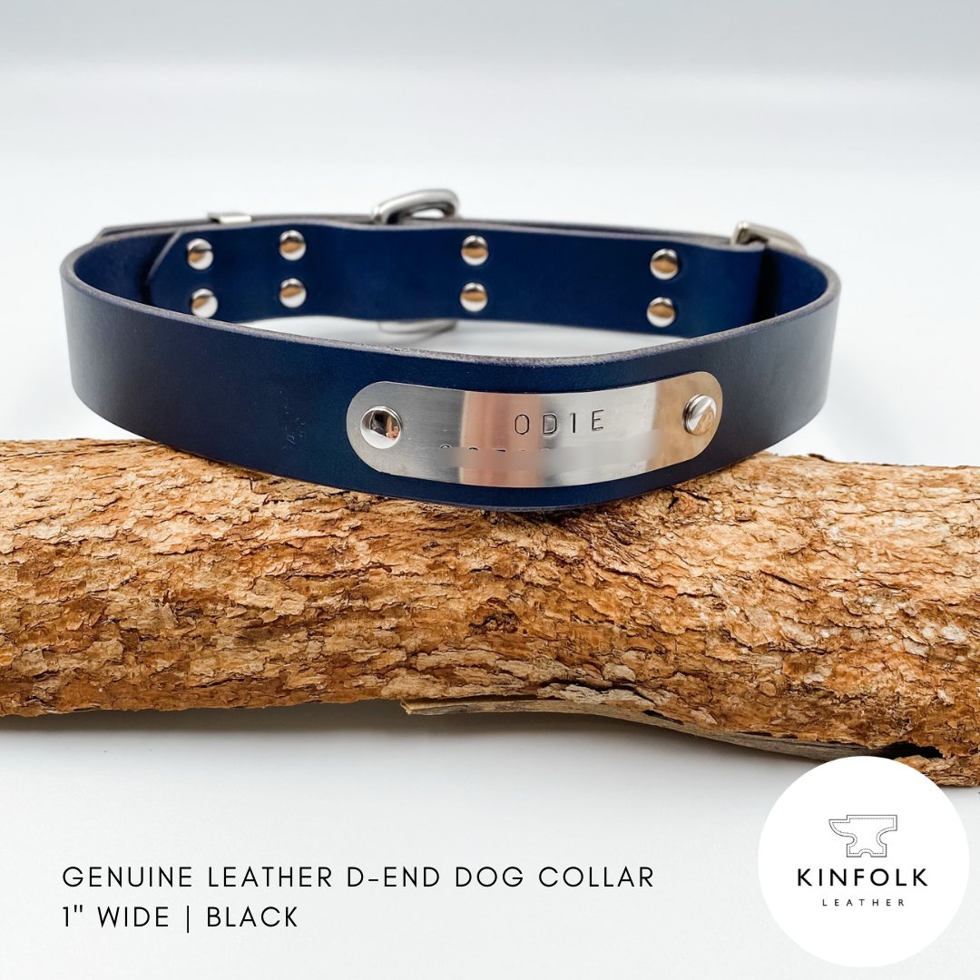 Black leather dog collar with a silver nameplate on a wooden log, branded 'KINFOLK LEATHER'.