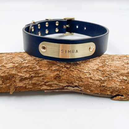 Navy blue leather dog collar with gold nameplate on a wooden log