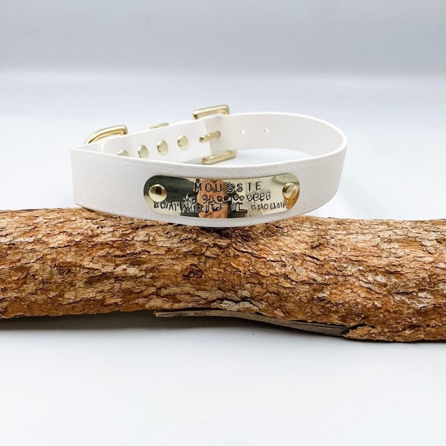 White dog collar with gold hardware on a wooden log against a light gray background